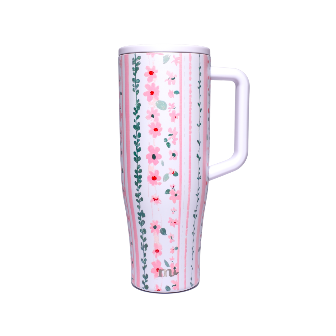 A tall travel tumbler with a floral and striped pattern, featuring pink flowers, green vines, and vertical pink stripes on a white background, with a white handle and lid.