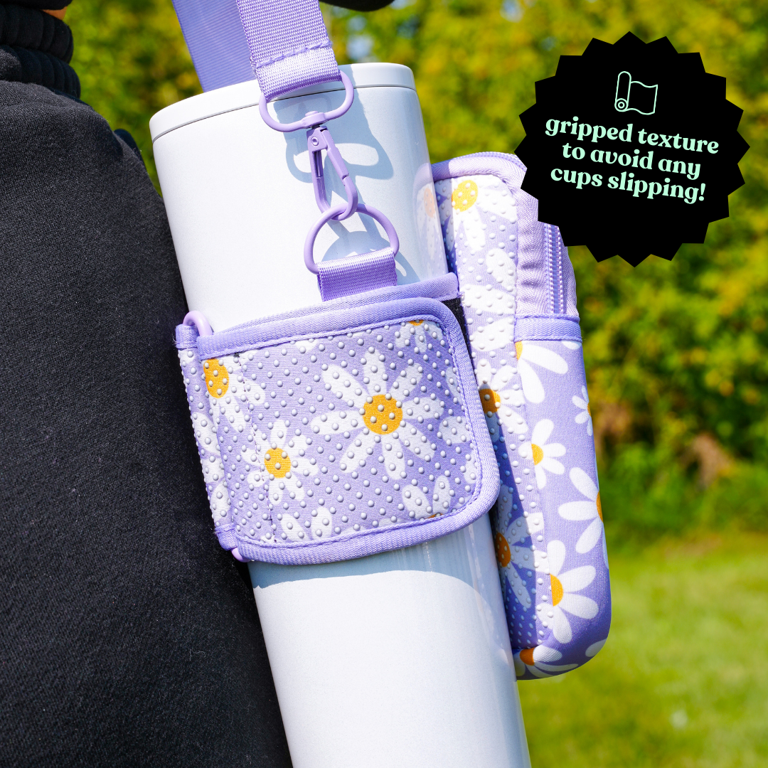 30 oz Pearl Tumbler in a Purple Daisy Sling with Gripped Texture - The tumbler is securely held in a purple floral sling with a gripped texture to prevent slipping. The daisy pattern pouch provides additional storage while the adjustable strap makes it easy to carry, perfect for hands-free convenience during outdoor activities.