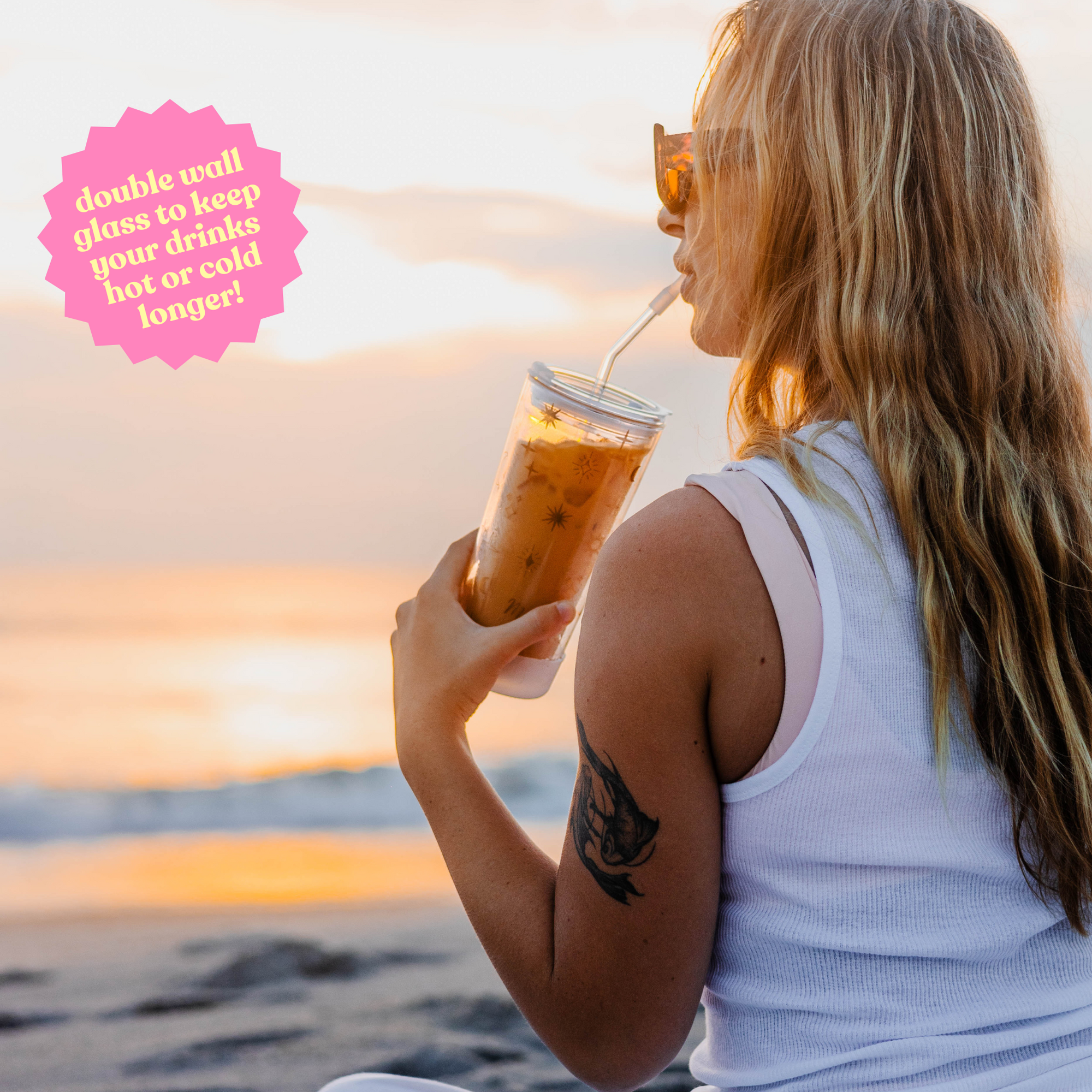 Woman drinking from a 20oz double-wall glass cup with celestial design at sunset, with text: 'Double wall glass to keep your drinks hot or cold longer!