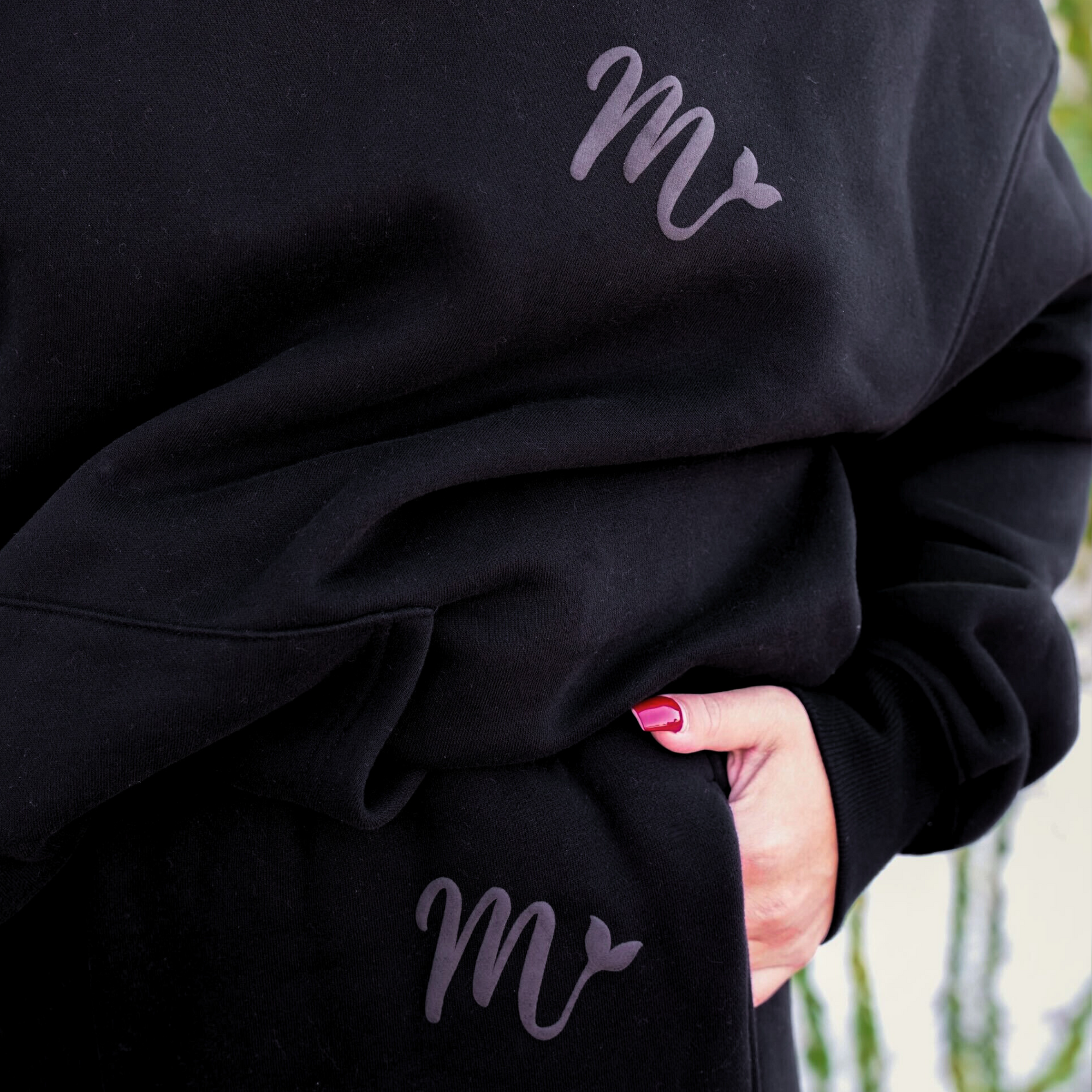 Close-up of a black hoodie and matching sweatpants set with a subtle embossed logo on both the hoodie and pants. The design showcases the raised 'M' logo, adding a stylish and unique touch to the cozy, casual outfit.